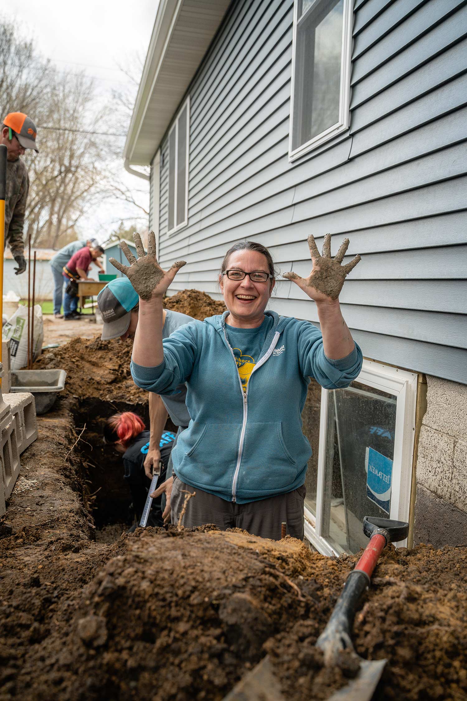volunteer in dug hole laughing while showing dirt on hands