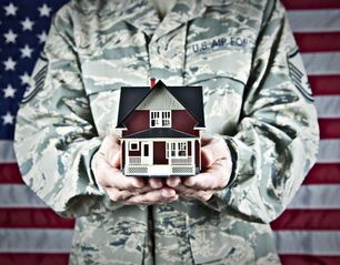 Person in army clothing holding a model of a small house