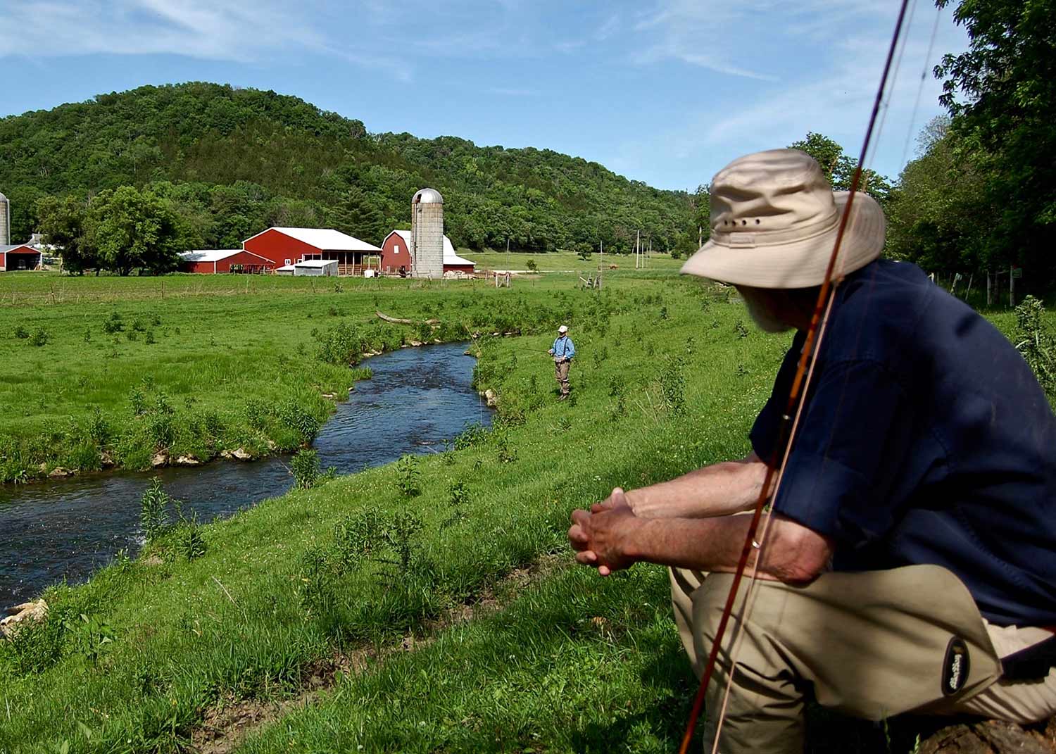 man fishing on creek near farmland